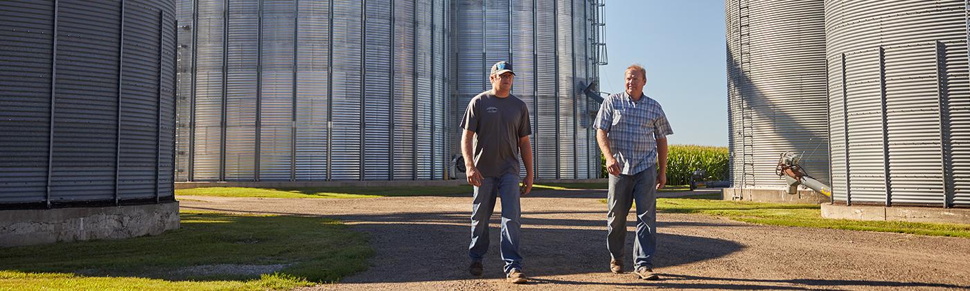 two farmers walking between grain silos on a sunny day